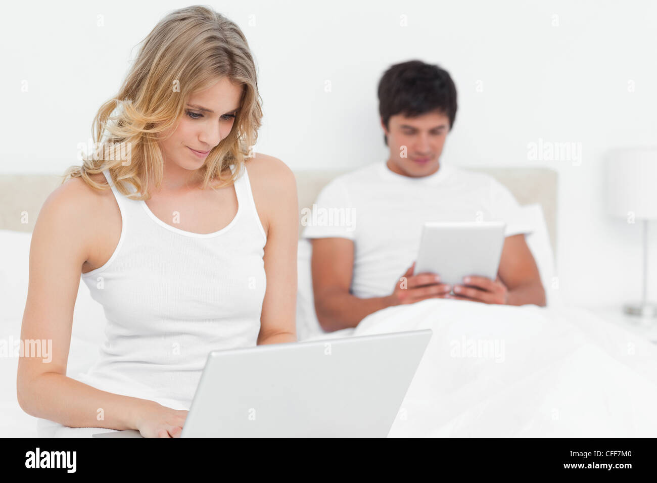 Frau mit einem Laptop und der Mann mit einem Tablet an entgegengesetzten Enden der Bett lächelnd Stockfoto