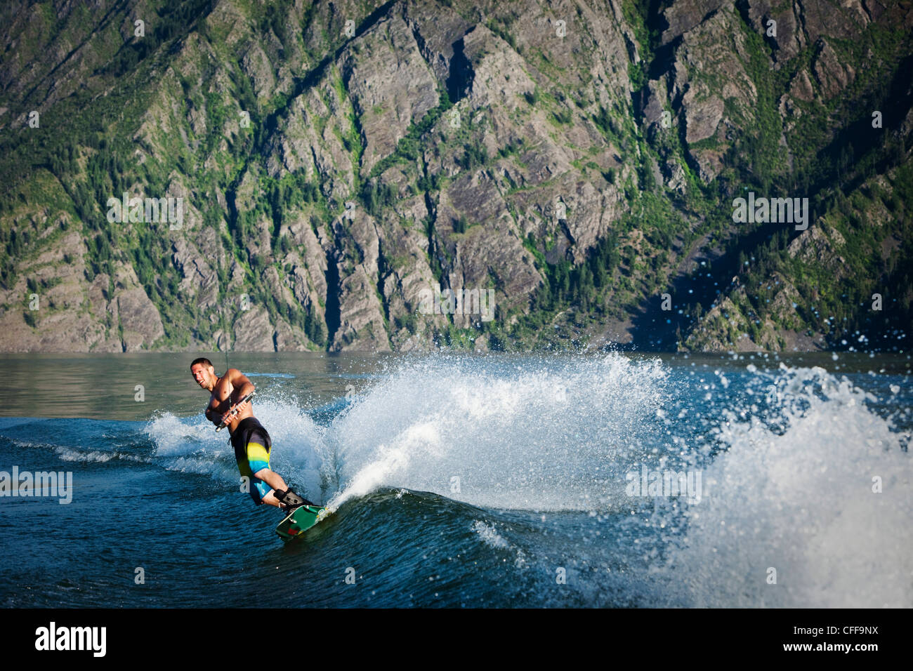 Eine sportliche männliche Wakeboarder schnitzt und Slahes Gefolge bei Sonnenuntergang an einem See in Idaho. Stockfoto