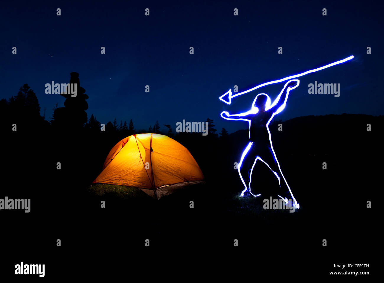 Lightpainting eines Mannes schwebend einen Speer über seinem Kopf neben einem glühenden Zelt bei Sonnenuntergang in Idaho. Stockfoto