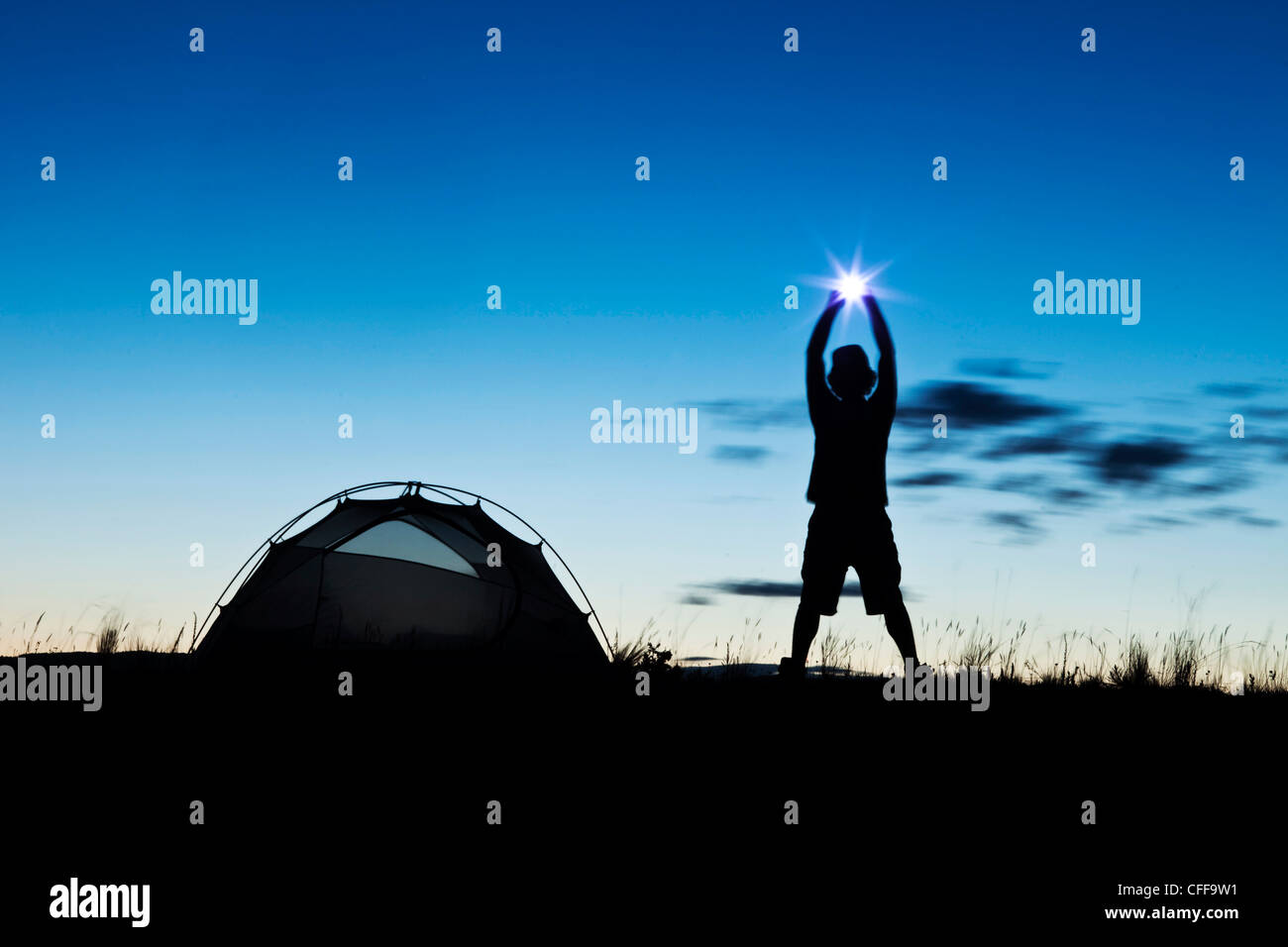 Ein Mann steht, hält einen Stern neben seinem Zelt bei Sonnenuntergang auf einem camping-Ausflug in Montana. Stockfoto