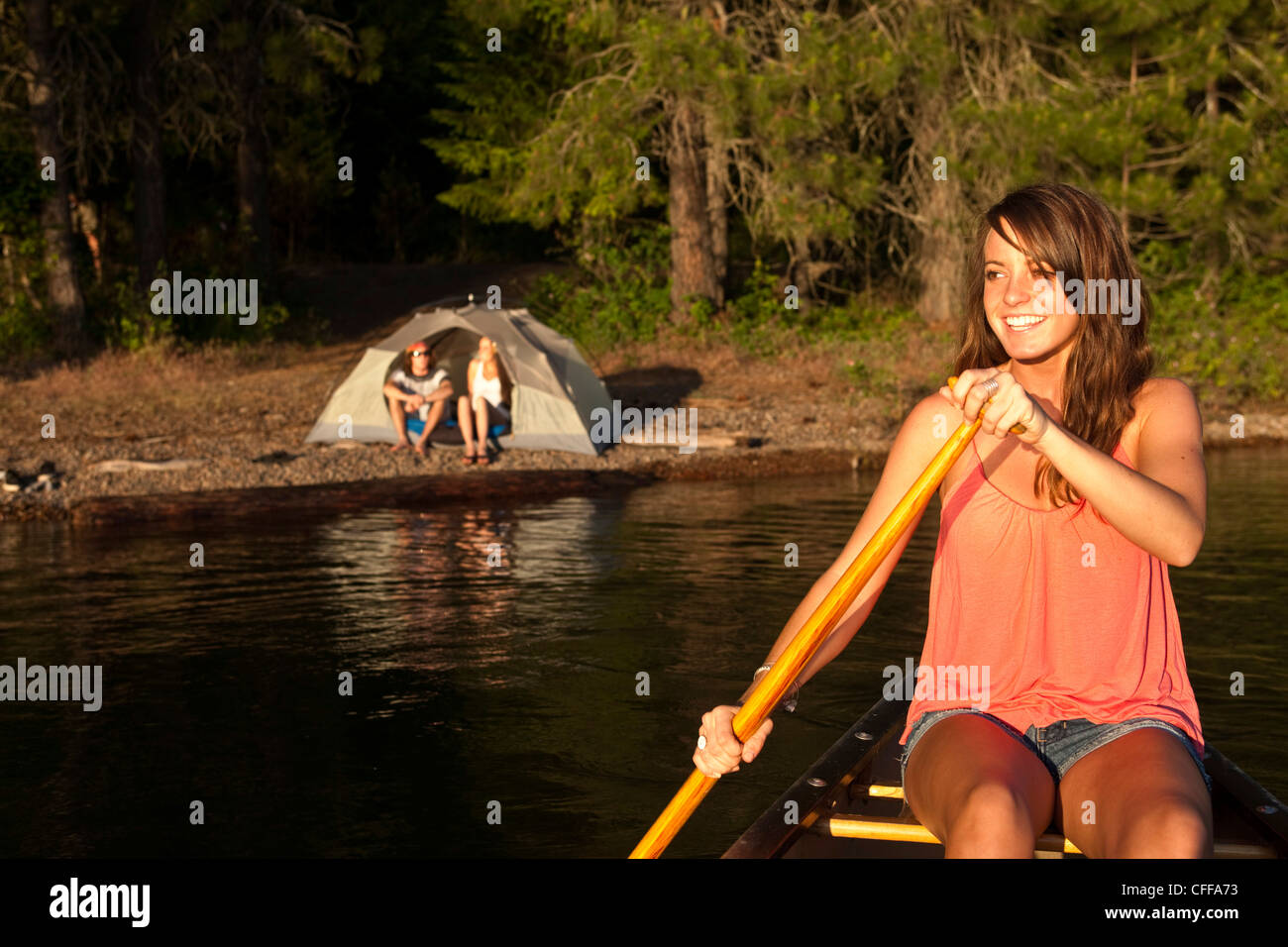 Eine glückliche junge Frau lächelt beim Kanufahren auf einem camping-Ausflug auf einem See in Idaho. Stockfoto