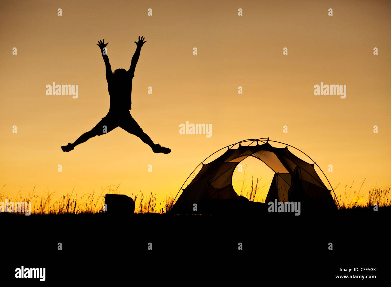 Ein Mann springt neben seinem Zelt bei Sonnenuntergang auf einem camping-Ausflug in Montana. Stockfoto