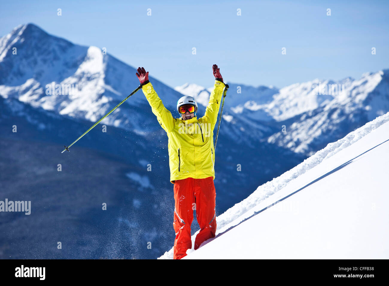 Skifahrer glücklicher lächelnd wirft seine Arme in der Feier der Neuschnee mit riesigen Bergen hinter ihm in Colorado. Stockfoto