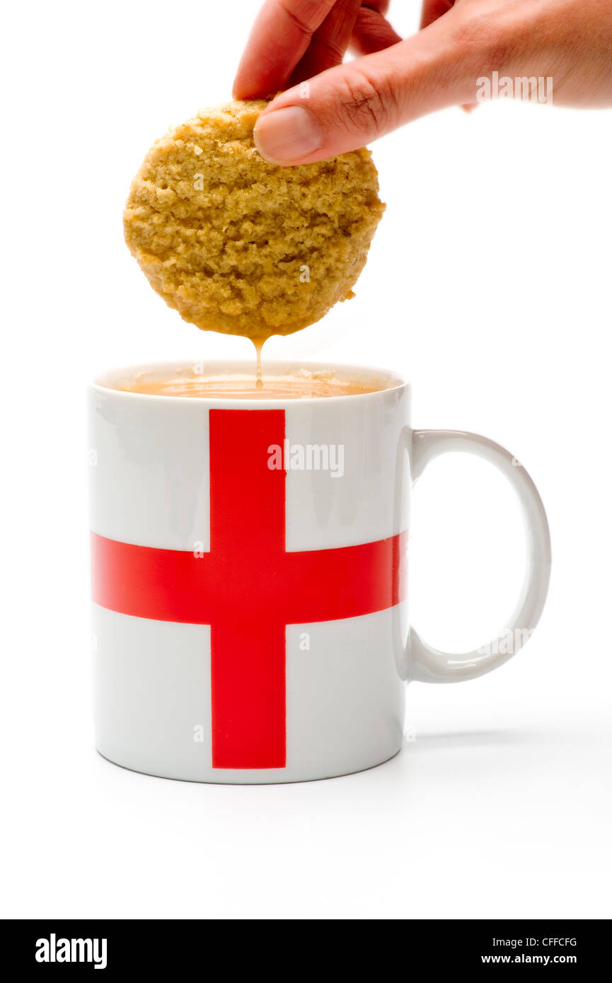 Kaukasische Hand, die einen entunkenen Keks aus einer Tasse Tee mit der englischen Flagge hebt. Stockfoto