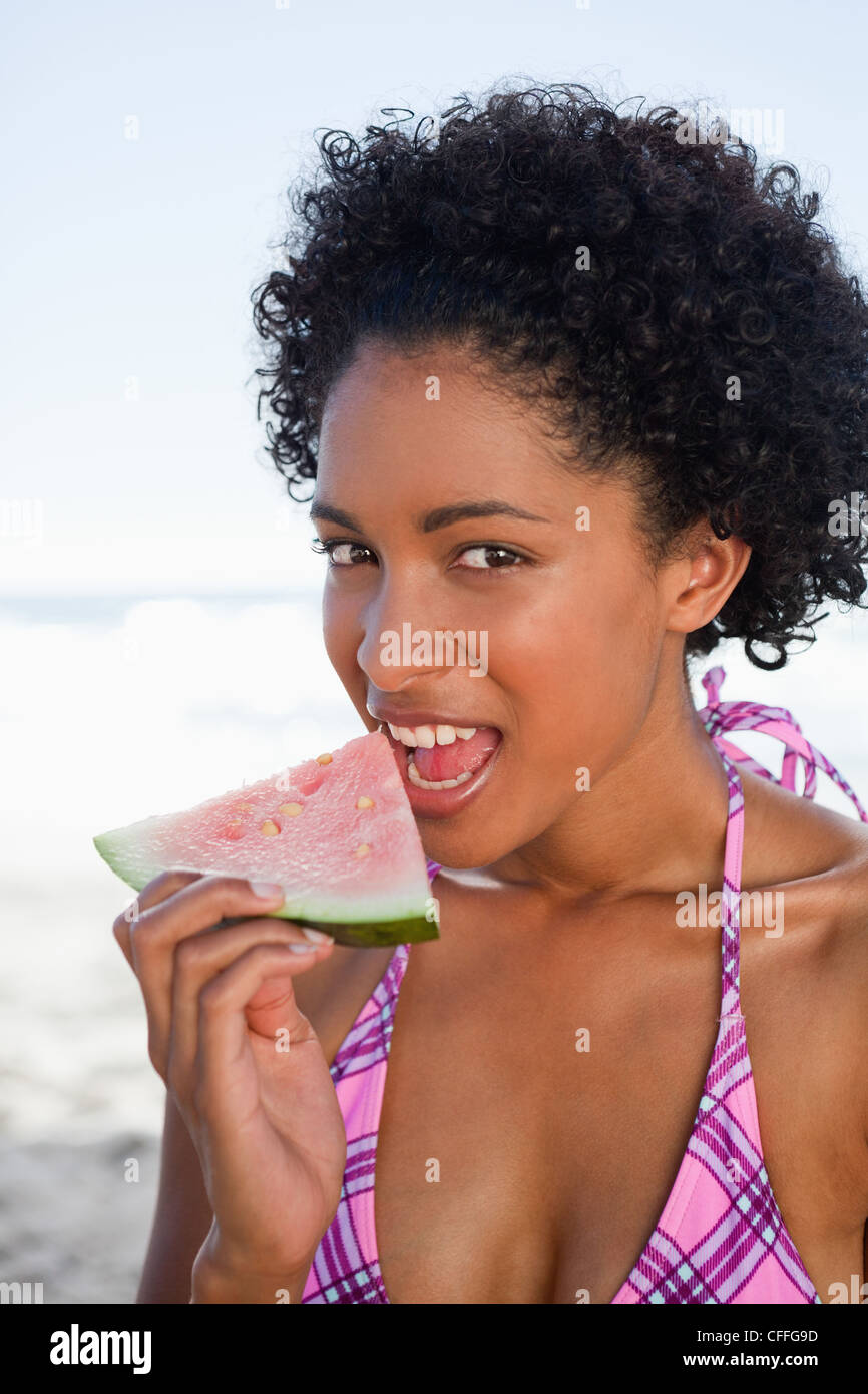 Junge attraktive Frau schaut in die Kamera während des Essens ein Stück Wassermelone Stockfoto