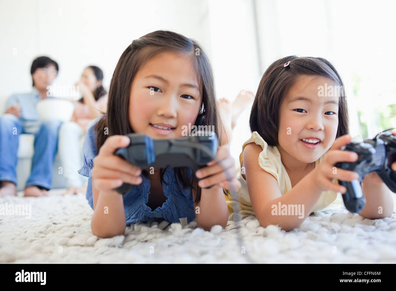 Die Mädchen spielen ein Videospiel, während die Eltern sehen und Essen Stockfoto