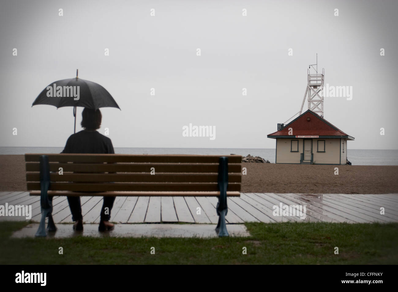 Mann mit Schirm sitzen auf Bank, Woodbine Strand, Toronto, Ontario Stockfoto