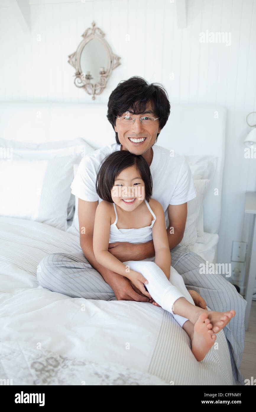 Ein Mädchen mit ihrem Vater hielt sie, wie sie Lächeln und auf dem Bett sitzen Stockfoto