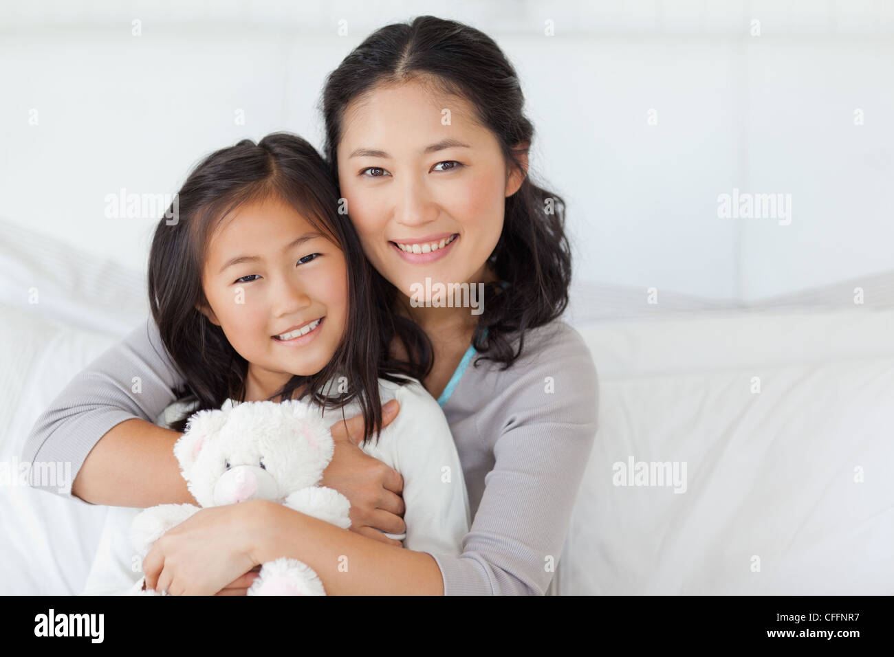 Eine Tochter und ihre Mutter umarmen einander auf dem Bett, wie das Kind einen Teddy hält Stockfoto