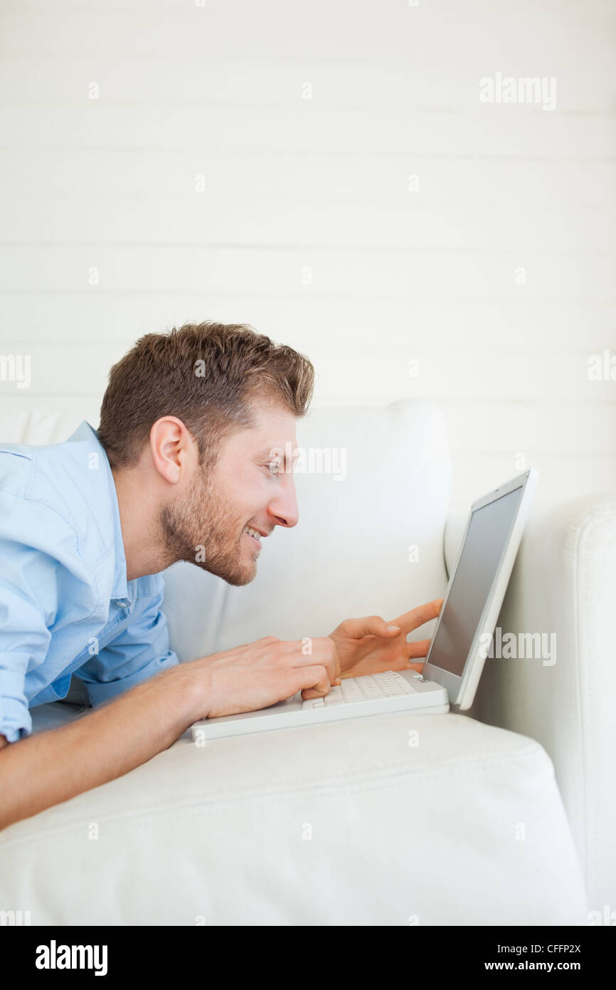 Mann mit seinem Laptop, wie er auf der Couch liegt und lächelnd Stockfoto