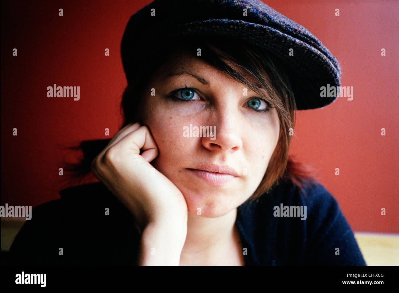 Porträt der Frau gegen rote Wand mit blauen Hut sitzt Stockfoto