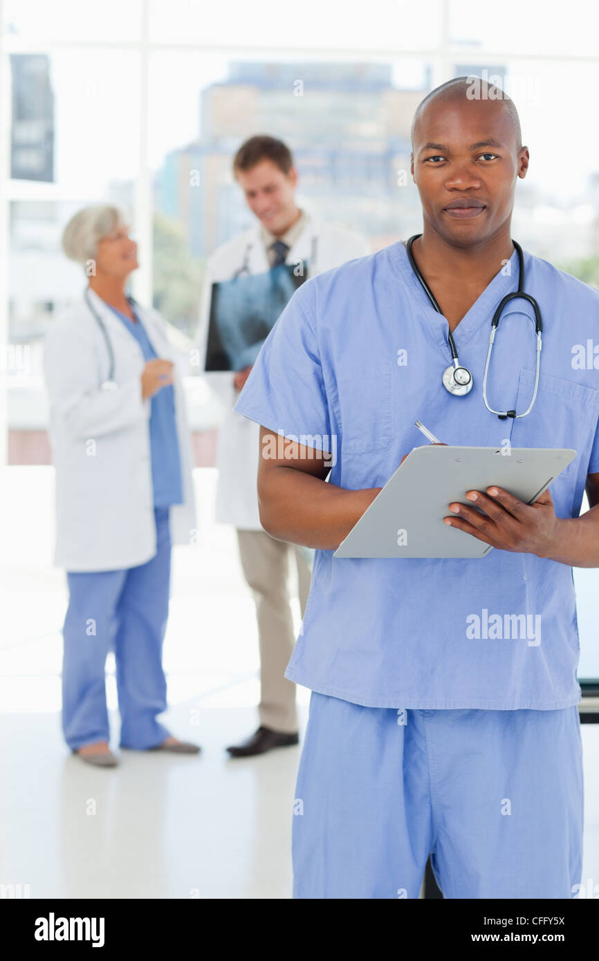 Arzt mit Zwischenablage und seine Kollegen hinter ihm Stockfoto