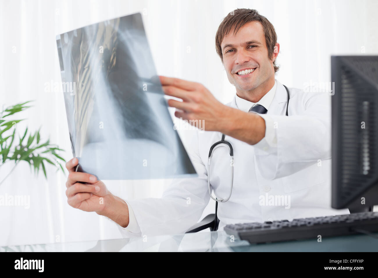 Lächelnde Arzt sitzt an seinem Schreibtisch ein Röntgen-Thorax mit gedrückter Stockfoto