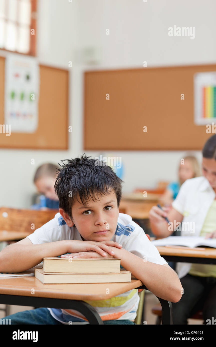 Traurig aussehende Student stützte sich auf einen Stapel Bücher Stockfoto