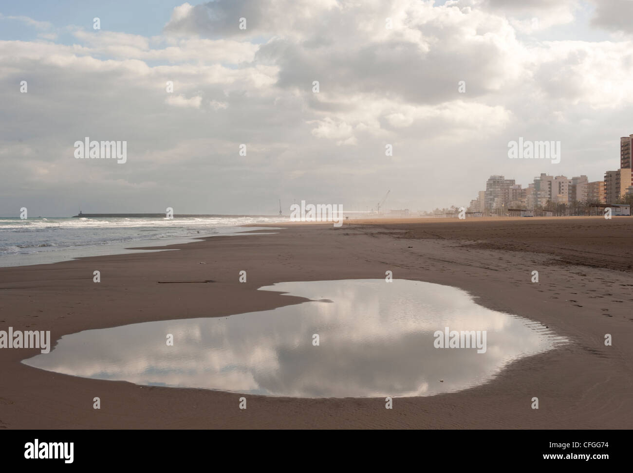 Eine große Pfütze spiegelt einen stürmischen bewölkten Himmel über dem Meer, als Regen im Winter auf den spanischen Ferienort von Gandia, Spanien setzt Stockfoto