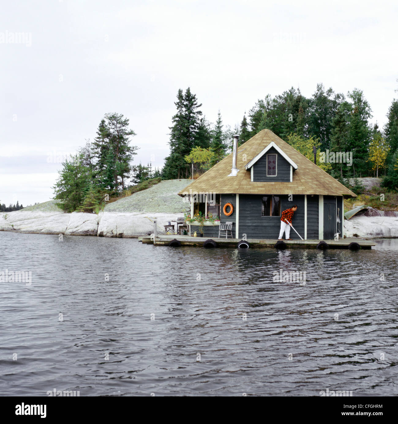 Mann mit Besen auf Kabine Dock von Lake, Lake Gunn, Minaki Ontario