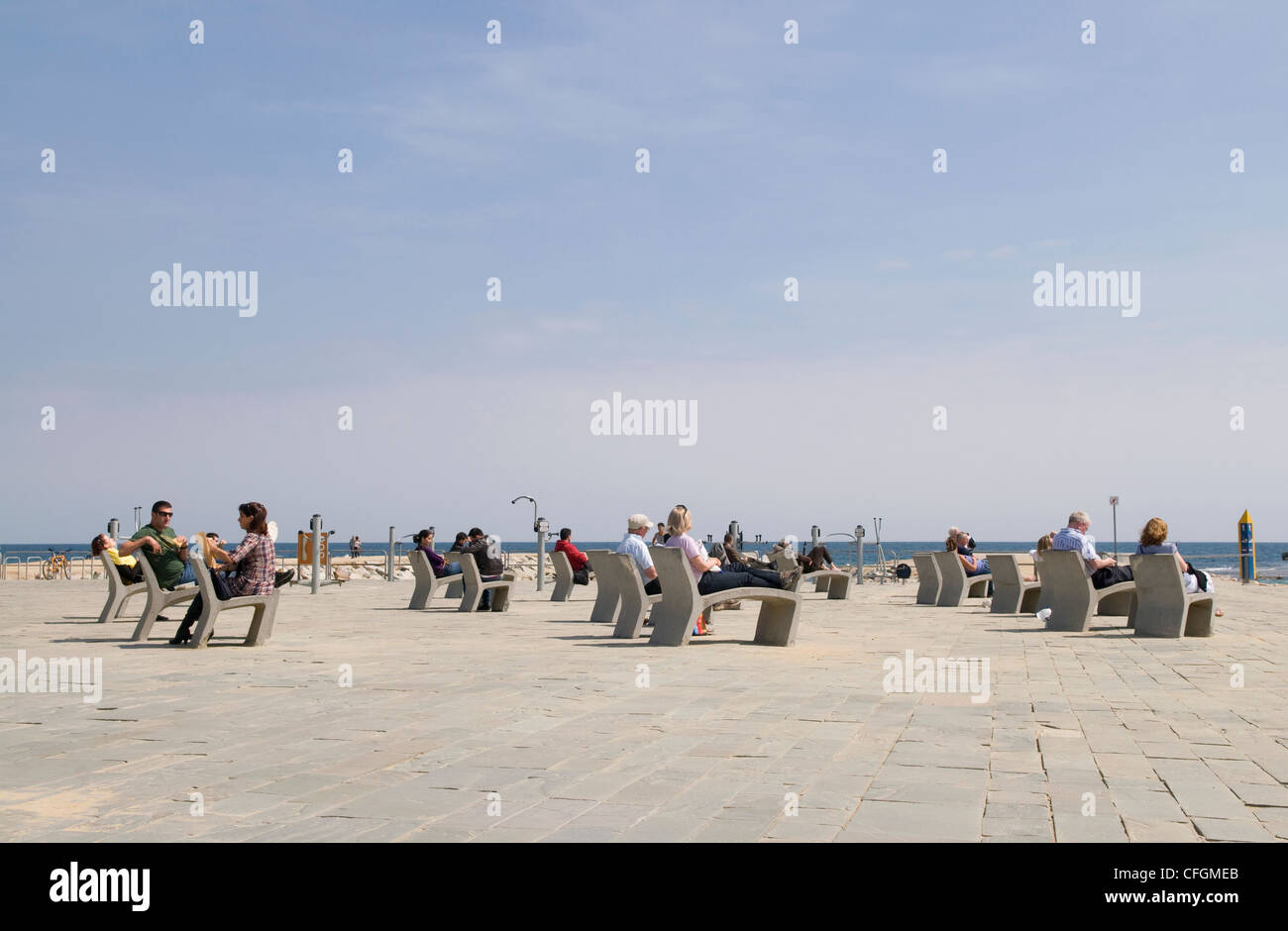 Menschen sitzen entspannt auf moderne Beton Stühle im Vordergrund des Meeres in Barcelona mit öffentlichen Fitnessgeräten im Hintergrund Stockfoto