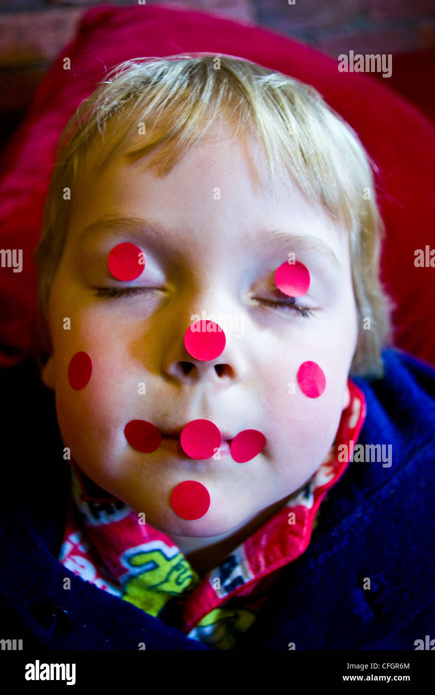 Ein Junge, der vorgibt, mit roten klebrige Punkte auf seinem Gesicht eingeschlafen zu sein. Stockfoto