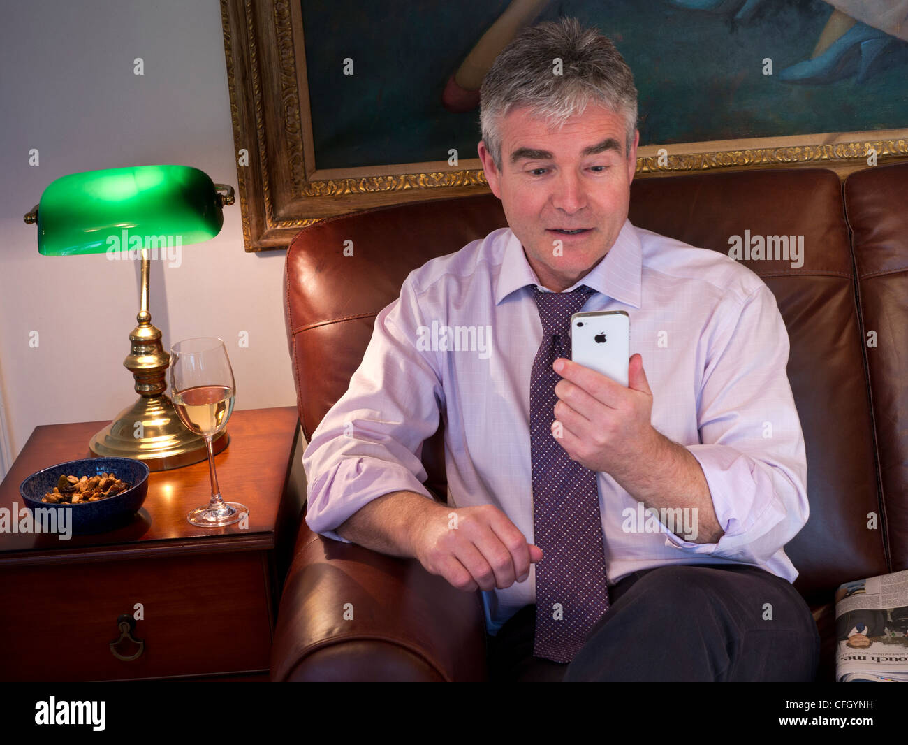 Geschäftsmann entspannend auf Ledersofa auf Bildschirm des weißen Smartphone Apple iPhone 4 s Stockfoto