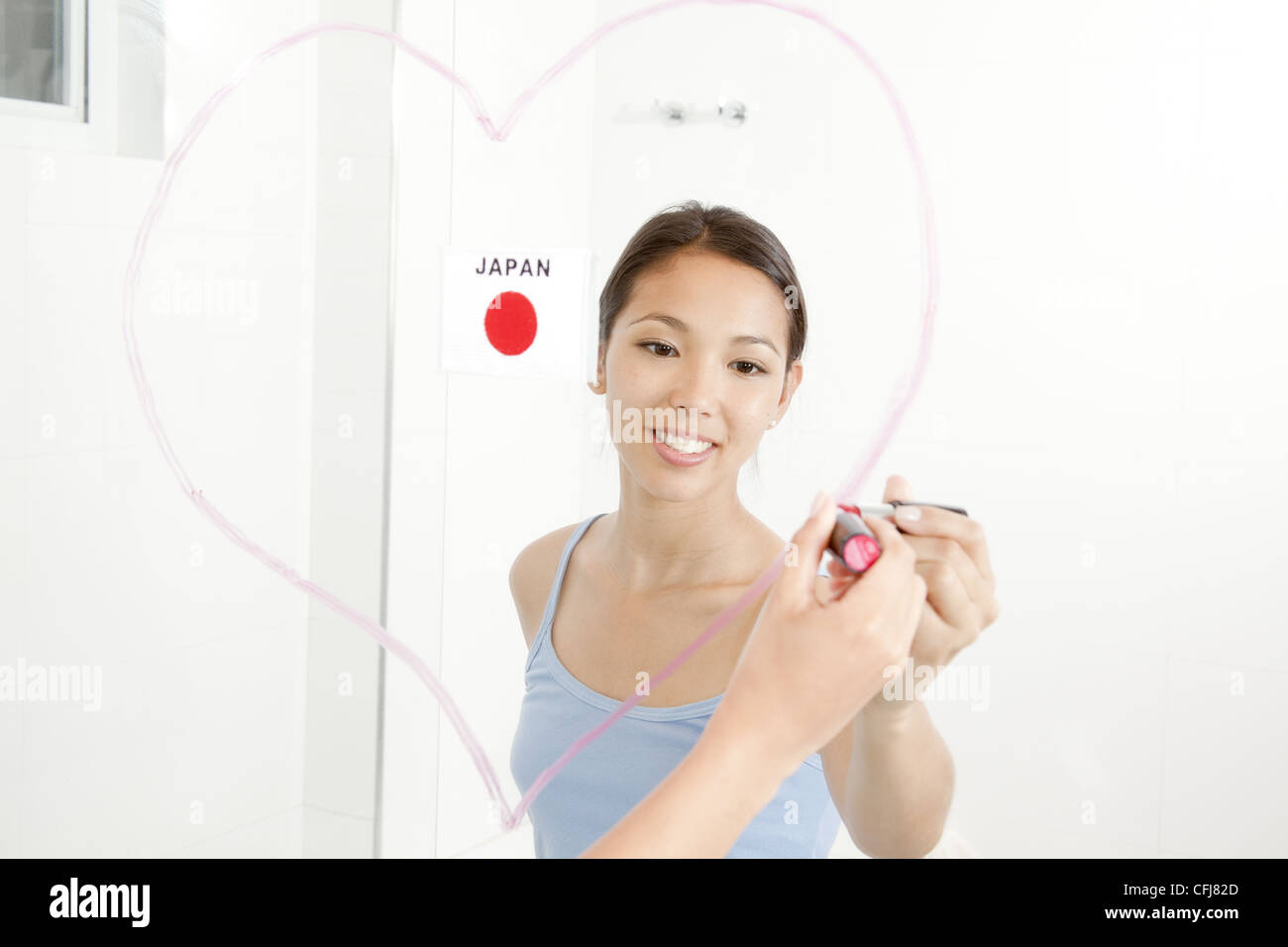 Junge Frau Herz mit Lippenstift auf den Spiegel zeichnen Stockfoto