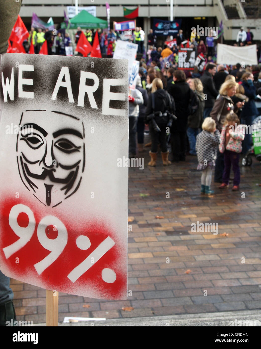 Wir sind 99 % Plakat mit dem Guy Fawkes Maske Symbol und Demonstranten im Hintergrund Stockfoto