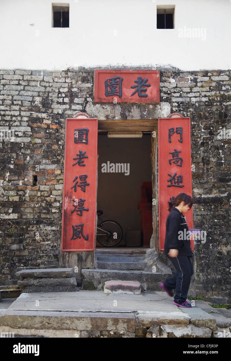 Frau zu Fuß aus der Tür des Lo Wai walled Village, Fanling, New Territories, Hong Kong, China, Asien Stockfoto