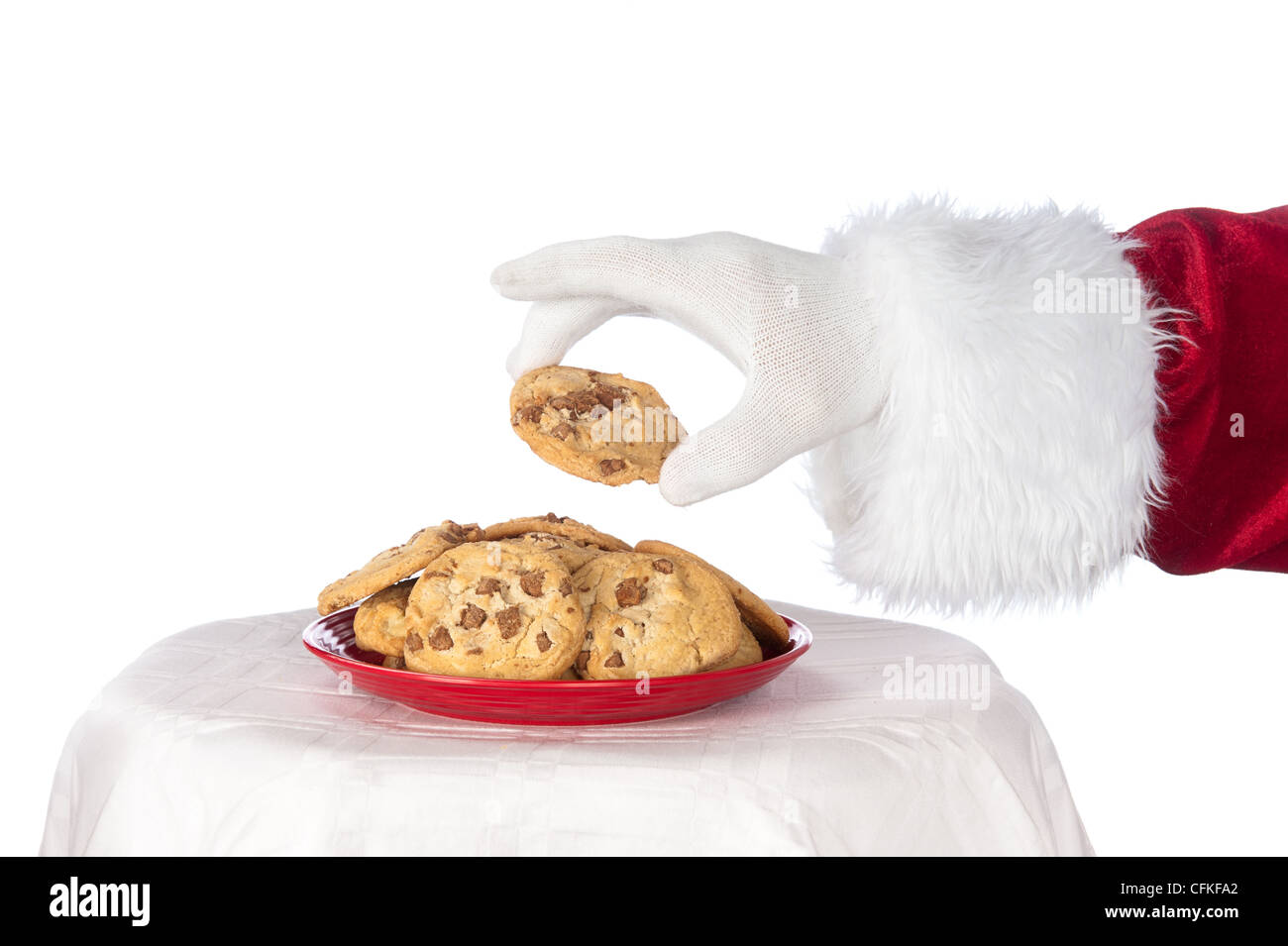 Santa Claus für eine frische chocolate Chip Cookie von einer roten Platte vor einem hellen, weißen Hintergrund erreichen Stockfoto