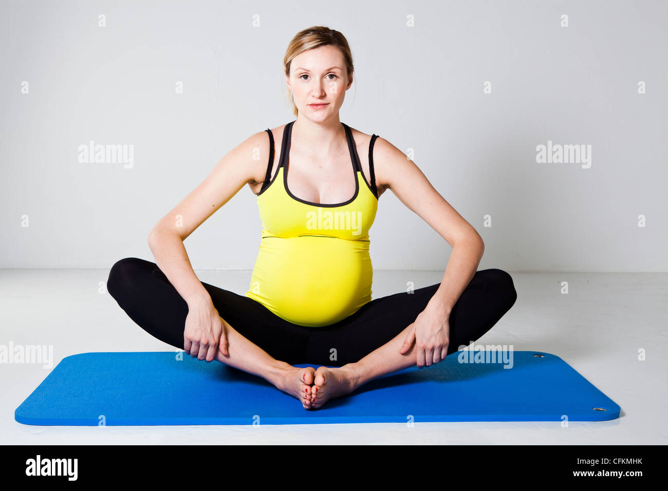 Schwangere Frau, die Durchführung einer inneren Oberschenkel Bein Strecken auf einer Matte Stockfoto