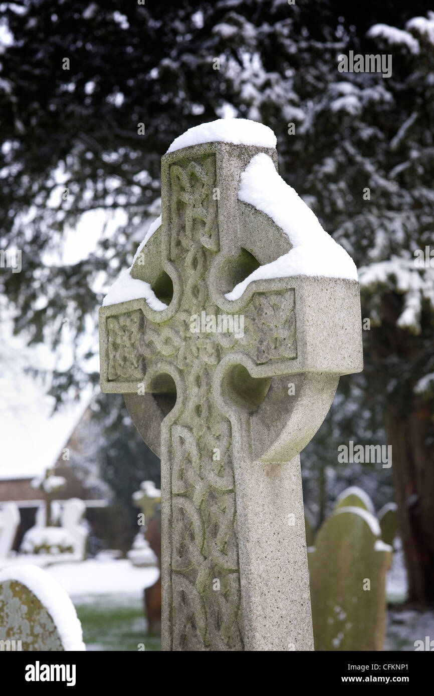 Schnee liegt auf einem Grabstein mit einem keltischen Muster, auf einem Friedhof. Stockfoto
