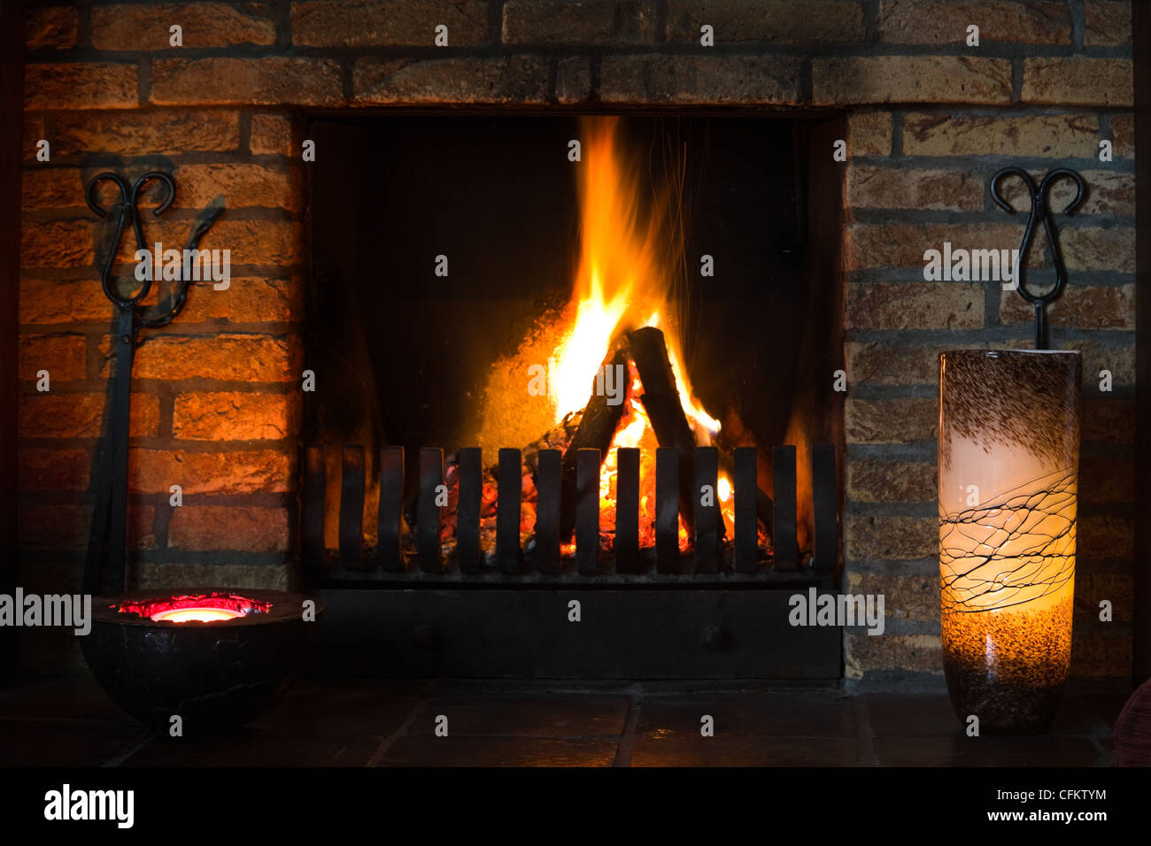 Offener Kamin im Wohnzimmer mit brennendem Holz und dekoriert mit Kerzen Stockfoto