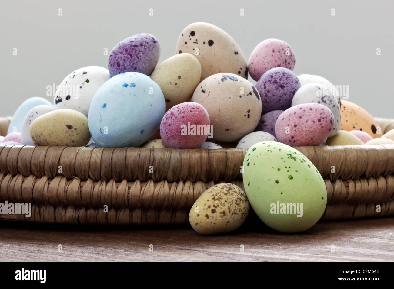 Still-Leben Foto gefleckte Süßigkeiten bedeckt Schokoladeneier in einem Weidenkorb auf einem rustikalen Holztisch. Stockfoto