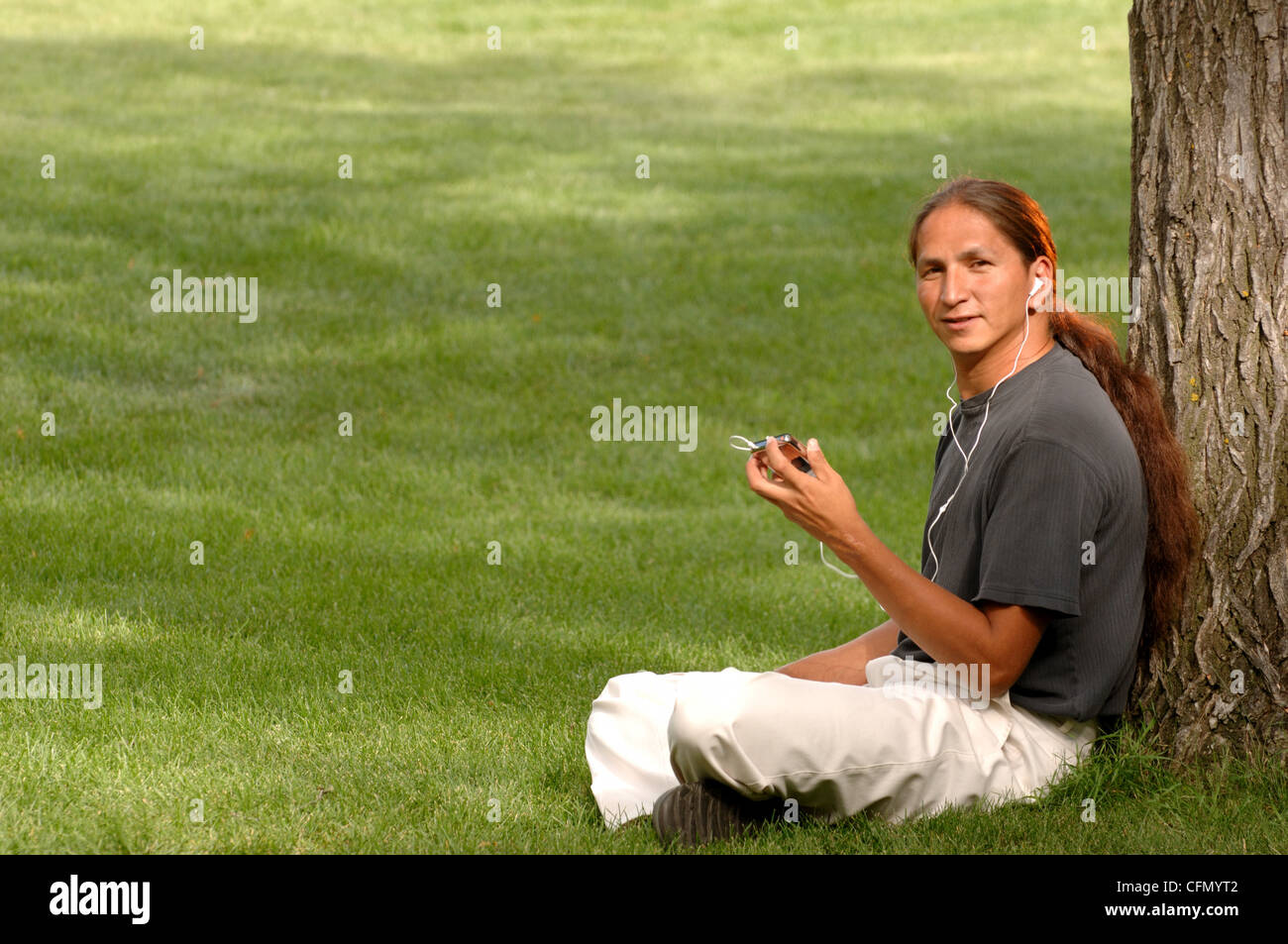 Mann sitzt auf dem Rasen, anhören von MP3-Player Stockfoto