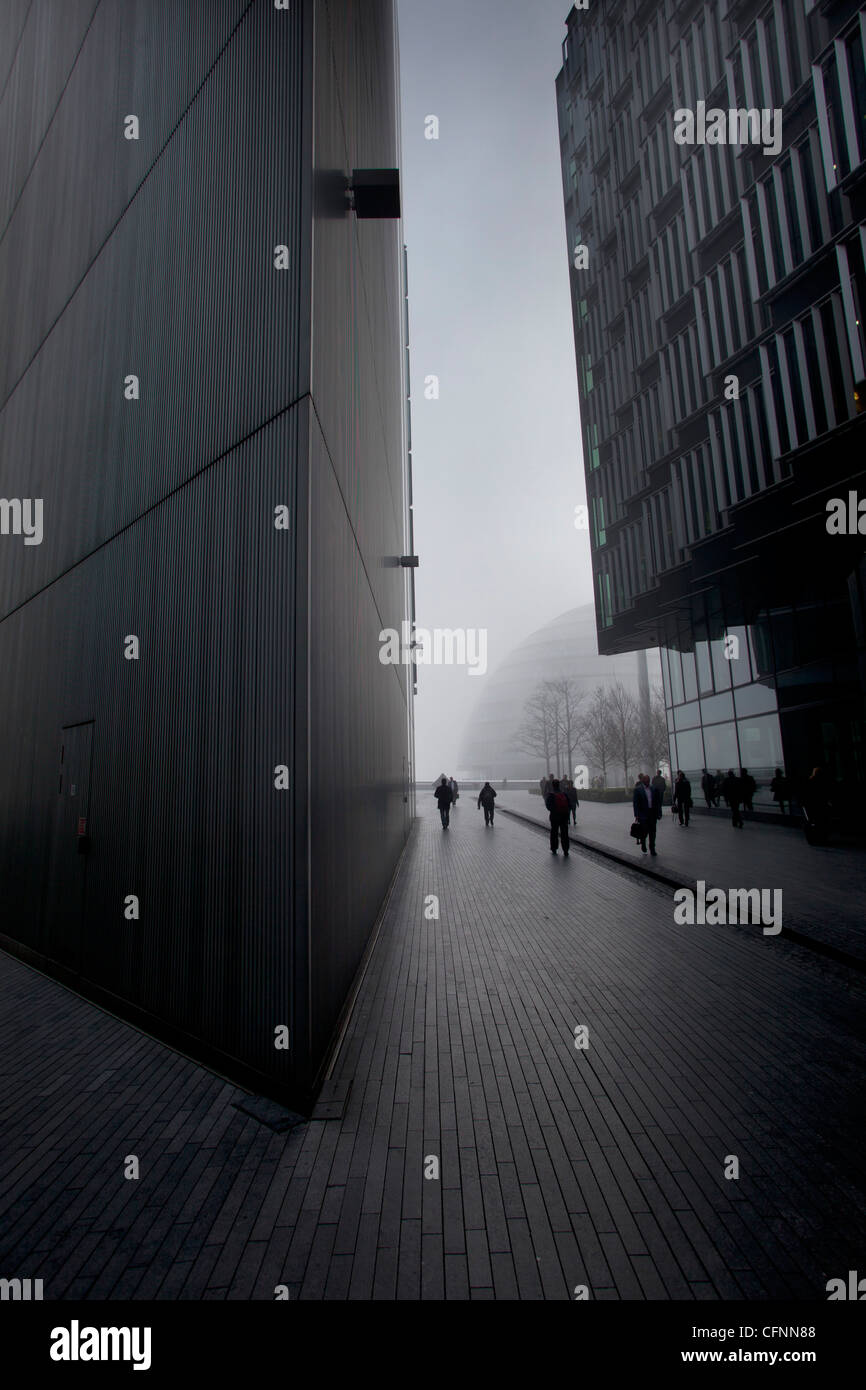 Pendler, die zu Fuß durch die Gebäude des Entwicklungsgebietes More London im Morgennebel Stockfoto