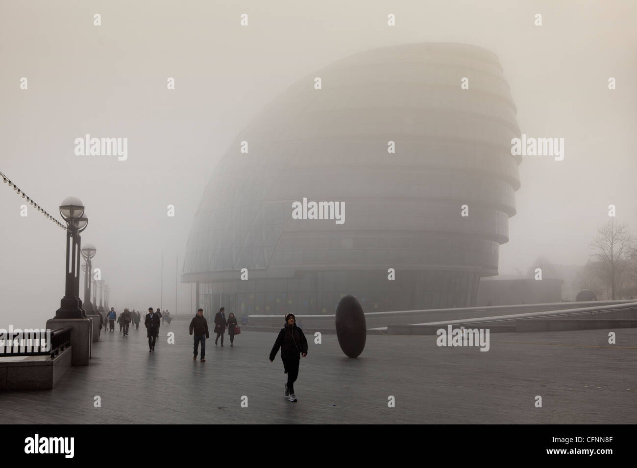 Pendler, die zu Fuß vorbei an London City Hall am Themse-Ufer im Morgennebel Stockfoto