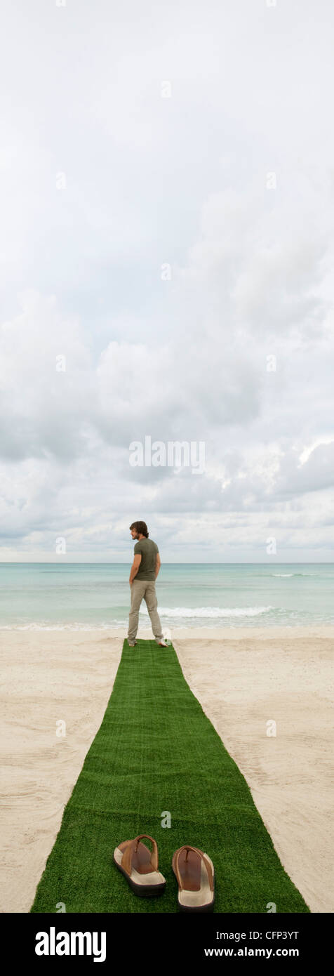 Mann stand am Ende der Teppich am Strand, Sandalen im Vordergrund Stockfoto