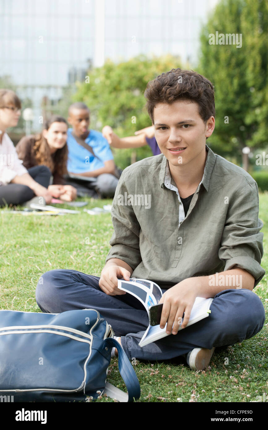 Junger Mann sitzt auf dem Rasen, Menschen im Hintergrund, Porträt Stockfoto