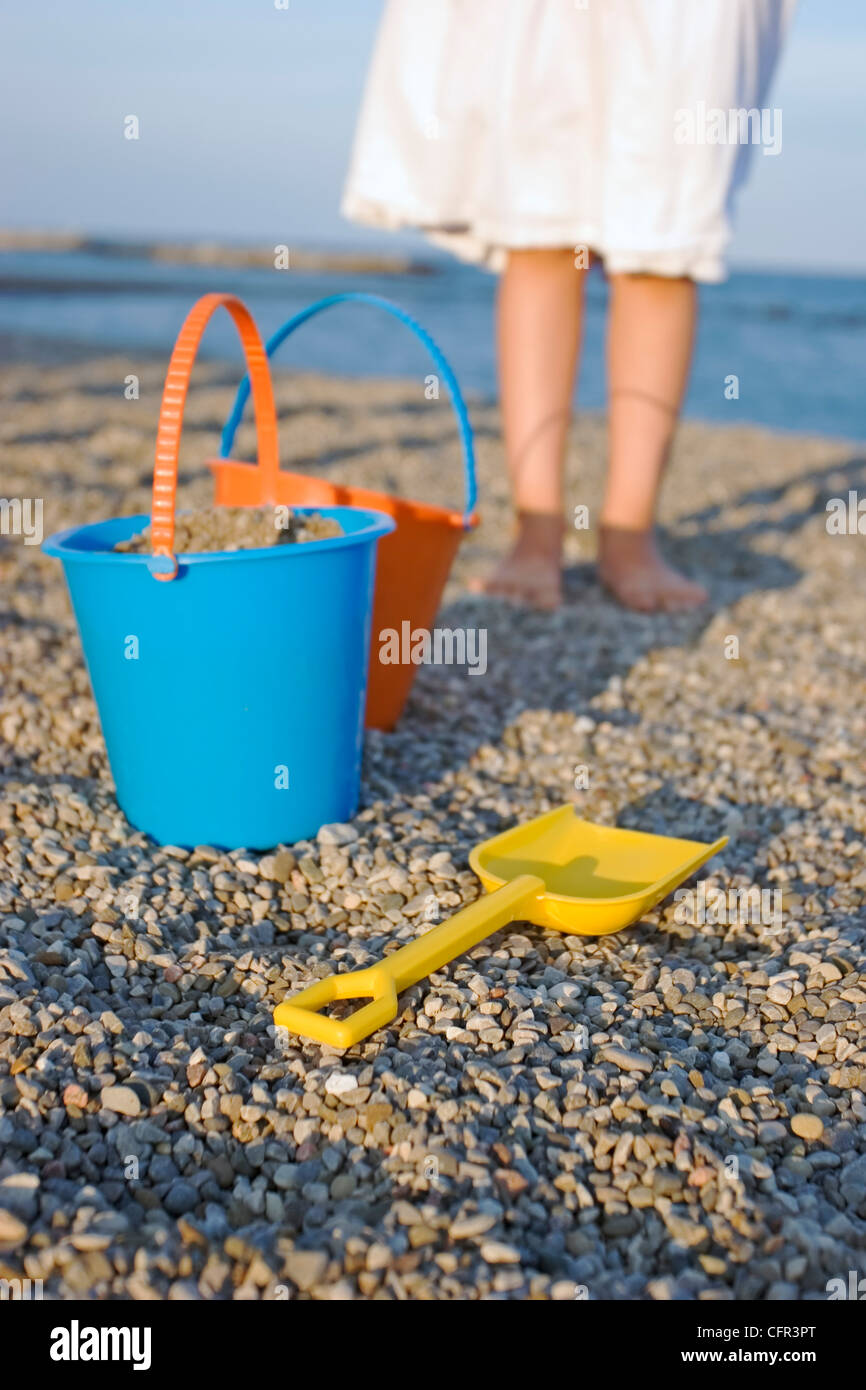 Eimer und Schaufel am Strand mit Mädchen Beine im Hintergrund Stockfoto