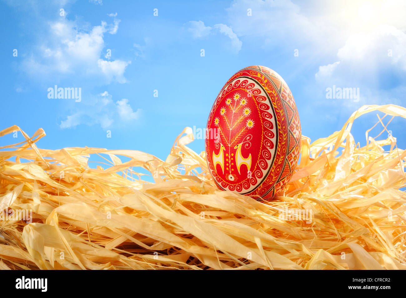 Easter Egg liegt auf strohgelb mit traditionellen ukrainischen Ornamenten bemalt. Sonnigen blauen Himmel mit Wolken im Hintergrund Stockfoto