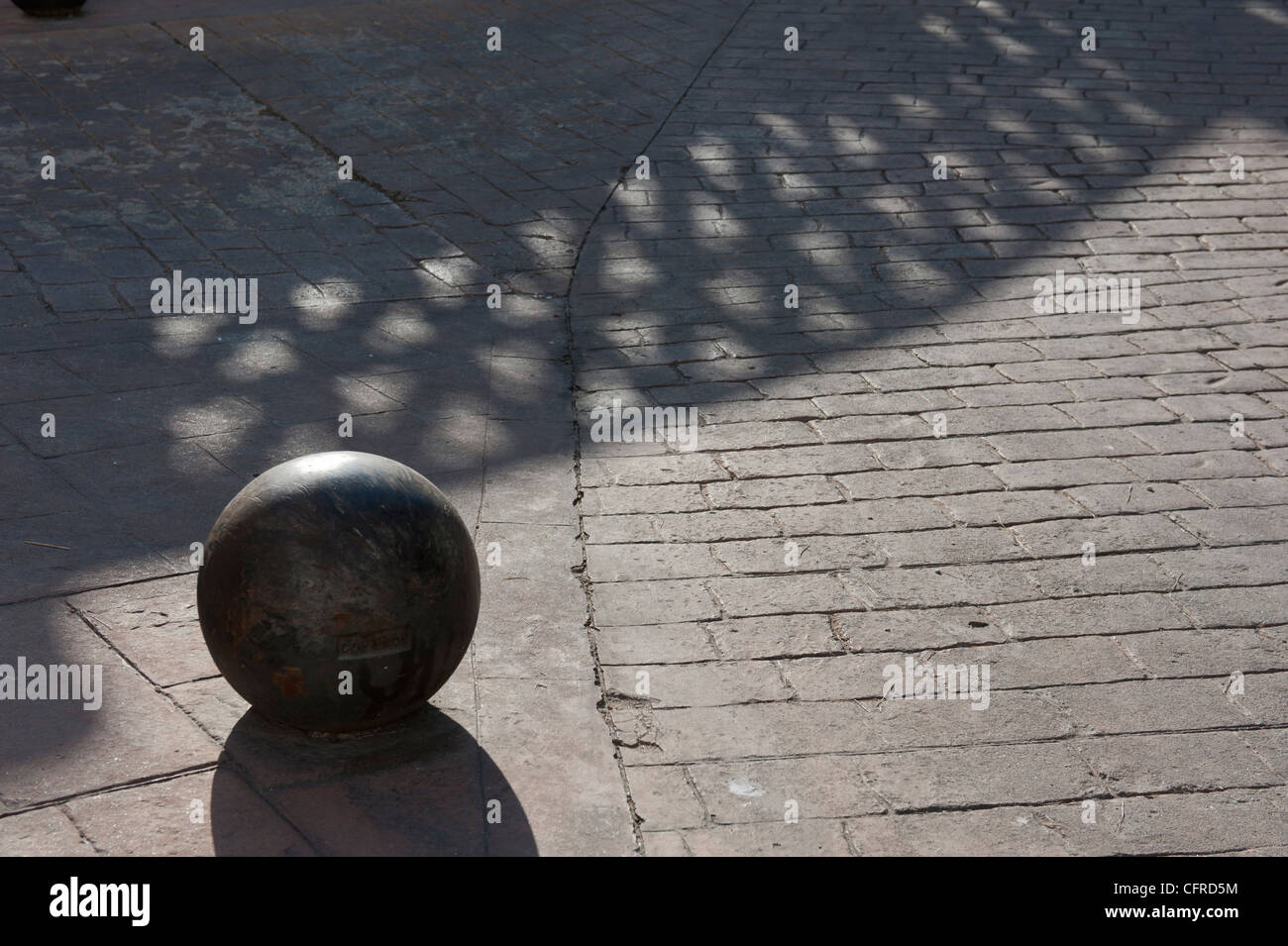 Stein Kugel auf Pflastersteine mit Schatten Muster der angrenzenden Zaun Stockfoto