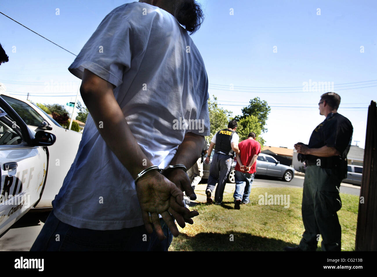 Mitglied einer mutmaßlichen Bande ist Hand gefesselt wie der andere ist weit entfernten Hintergrund, da beide Optionsscheine für ihre Verhaftung hatte. Strafverfolgungsbehörden aus in der gesamten Region beendet einen zweitägigen Sweep der Banden.  Bild 19. Juni 2007. Sacramento Bee Foto Bryan Patrick Stockfoto