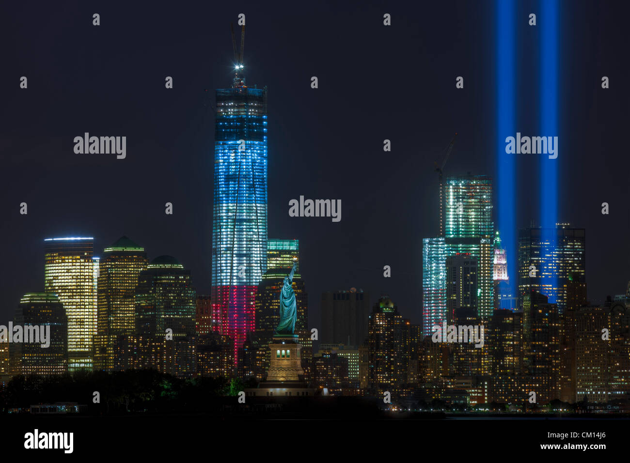 Die zwei Lichtstrahlen der Tribute in Light, eine jährliche Erinnerung an die Ereignisse des 11. September 2001, Leuchten in den Nachthimmel über der Skyline von lower Manhattan in New York City.  Dieser Blick auf die Skyline umfasst zwei Symbole der Freiheit, der Freiheitsstatue und der Freedom Tower (One World Trade Center). Stockfoto