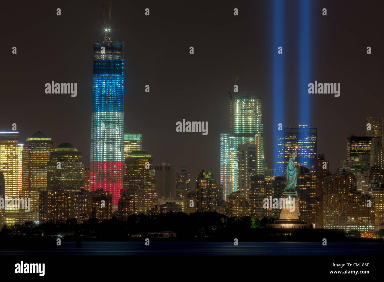 Die zwei Lichtstrahlen der Tribute in Light, eine jährliche Erinnerung an die Ereignisse des 11. September 2001, Leuchten in den Nachthimmel über der Skyline von lower Manhattan in New York City.  Dieser Blick auf die Skyline umfasst zwei Symbole der Freiheit, der Freiheitsstatue und der Freedom Tower (One World Trade Center). Stockfoto