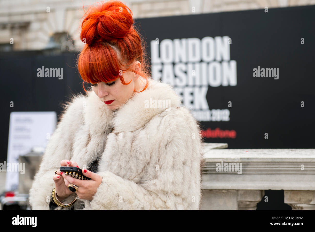 17. September 2012, UK. London Fashionweek im Somerset House, London. Die berühmte und modische besuchen die Shows oder rein zu hängen im Innenhof. Eine Frau mit orange Haare und Fell Jacke verwendet ihr Mobile Hinweistafel der London Fashion Week. Stockfoto