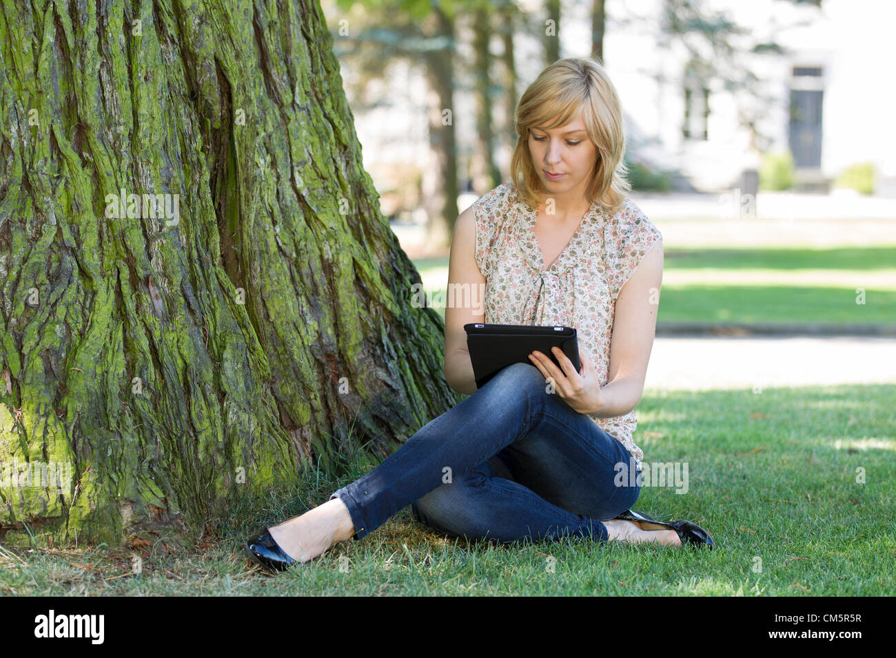 Casual Mädchen mit digital-Tablette von Baum auf Rasen Stockfoto