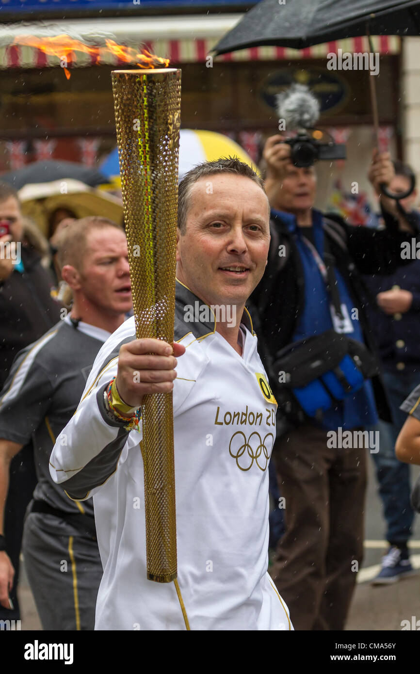 Northampton UK. 2. Juli 2012. Andy Wightman trägt die Olympische Fackel nach unten St Giles Street vor dem Guildhall Northampton Town Center, genauso wie der Regen beginnt. Stockfoto