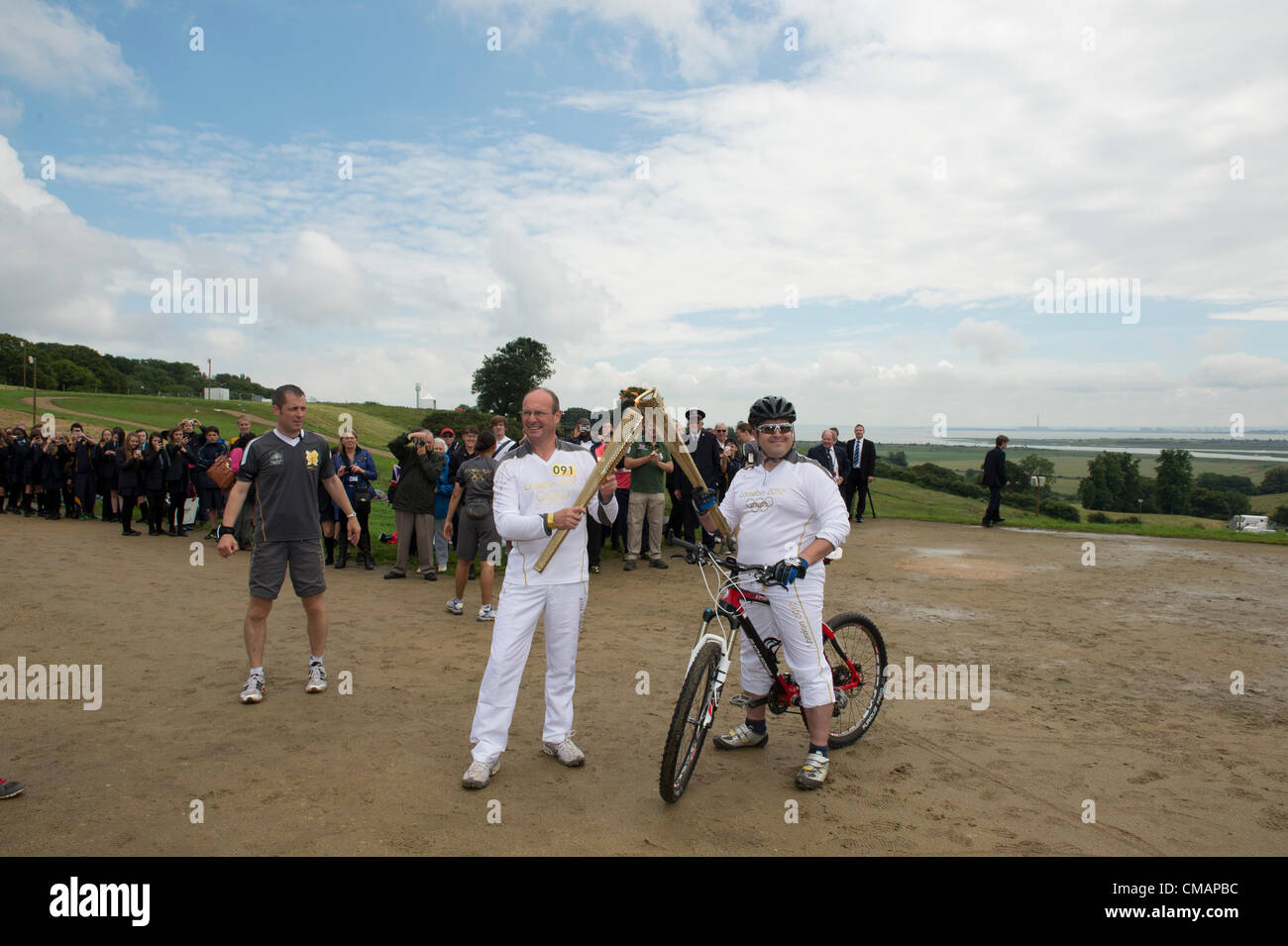 6. Juli 2012, Hadleigh Farm, Essex, England. Die Olympische Fackel durchläuft der Olympischen Mountainbike Ort wo Dan Jarvis (L) die Fackel um einen Abschnitt des Rennens nimmt route vor der Übergabe an Läufer Kim Axford (nicht abgebildet) und ab in Richtung Basildon und Grautöne. Das Wetter wurde zu trocken und sonnig, wie die Fackel am Veranstaltungsort angekommen. Stockfoto