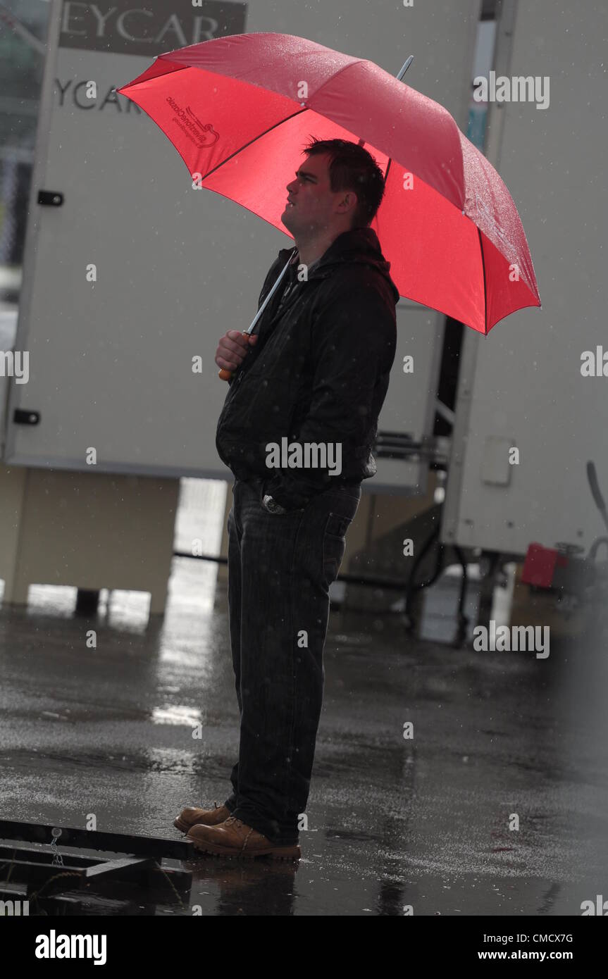20. Juli 2012, Silverstone im Vereinigten Königreich A Mann Schutz vor dem Regen unter einem roten Regenschirm wie der Regen fällt auf Silverstone Classic 2012 Stockfoto