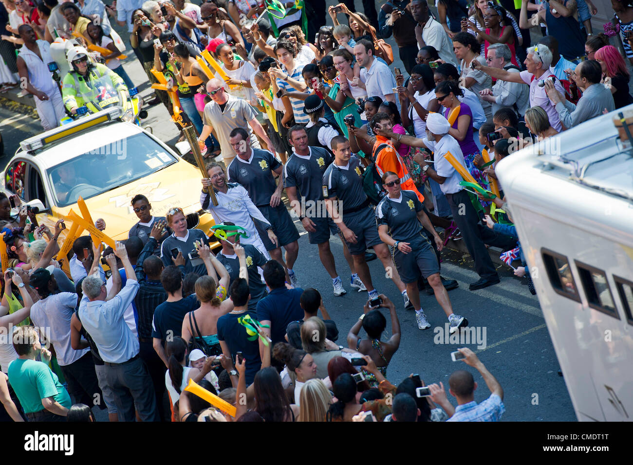 Der Olympische Fackellauf kommt Coldharbour Lane in Brixton, London, UK. Die Fackelträger durch die Polizei in der grauen Sportswear geschützt ist und das Relais ist von Sponsoren Fahrzeuge voraus. 26. Juli 2012. Stockfoto