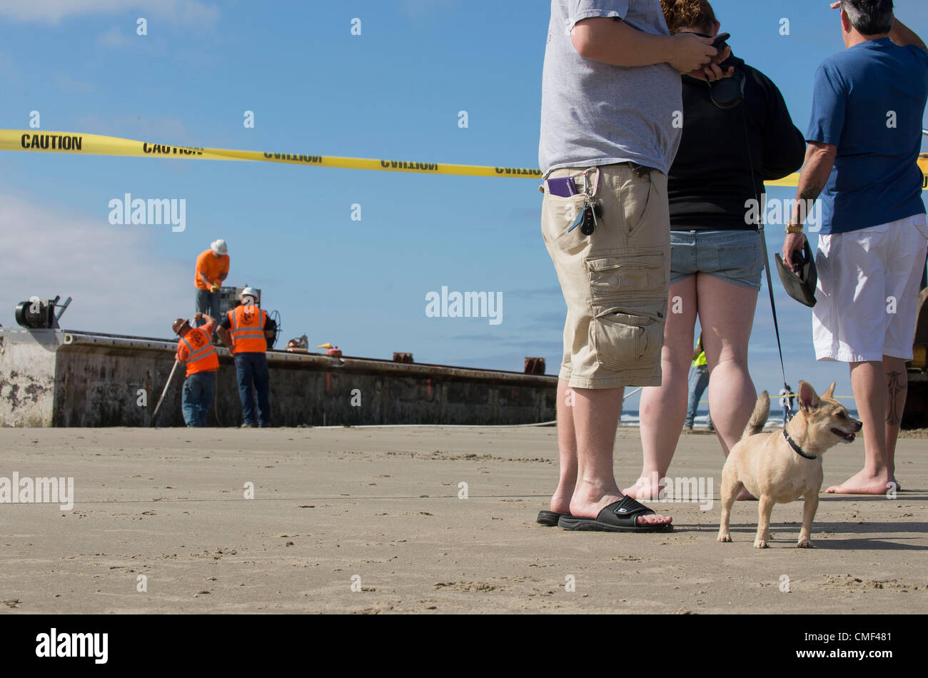 1. August 2012 - zusehen Newport, Oregon, USA - Touristen und ihr Hund, wie Arbeitnehmer beginnt den Prozess des Schneidens einer massiven gestrandet dock in Stücke auf Agate Beach in der Nähe von Newport.  Die riesigen japanischen Dock wurde vom letztjährigen Tsunami weggerissen und vor fast zwei Monaten an einer Oregon Strand gespült. Der japanischen Tsunami riss das Dock im März 2011 Lose aus ihrer Verankerung in der nördlichen japanischen Misawa. Eine 15-Monats-Odyssee über den Pazifik endete am 5. Juni bei einer Flut. (Bild Kredit: Robin Loznak/ZUMAPRESS.com ©) Stockfoto