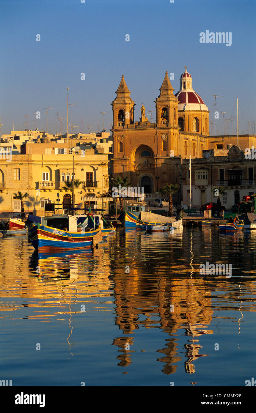 Hafen Sie mit Fischerbooten Luzzu und Marsaxlokk Pfarrkirche am Sonnenaufgang, Marsaxlokk, Malta, Mittelmeer, Europa Stockfoto